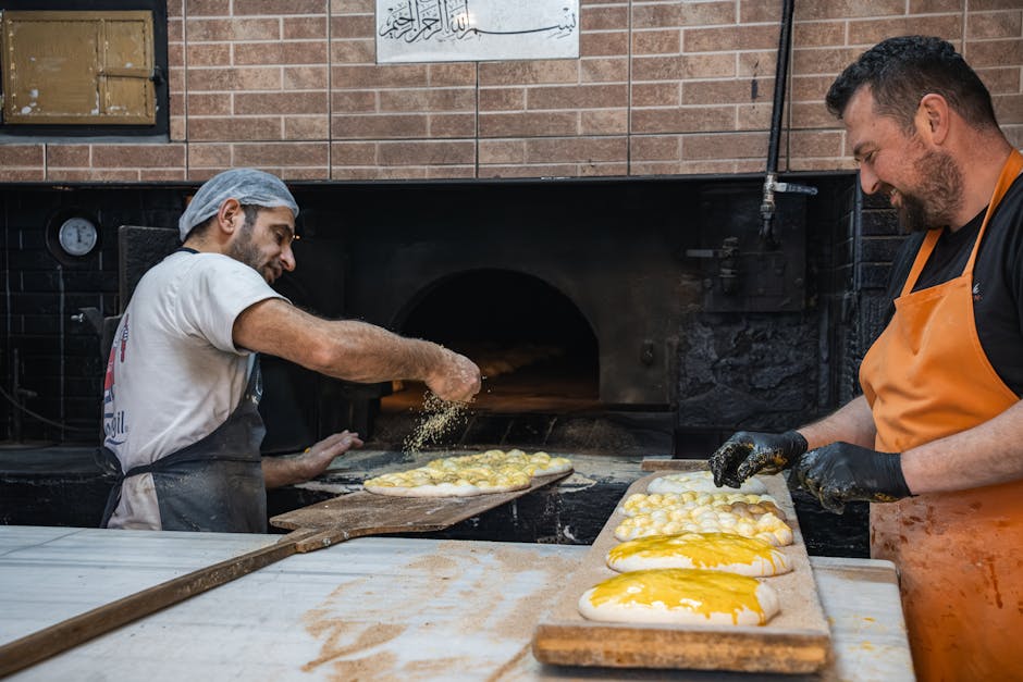 Two bakers prepare traditional Middle Eastern bread in a brick oven.