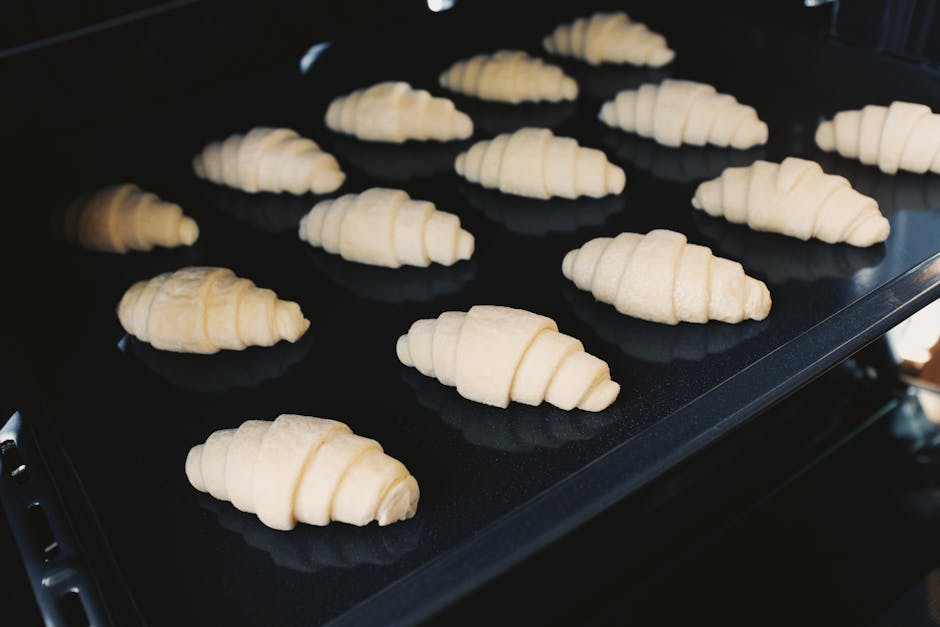 Close-up of uncooked croissants on a baking tray in an oven, captured indoors.