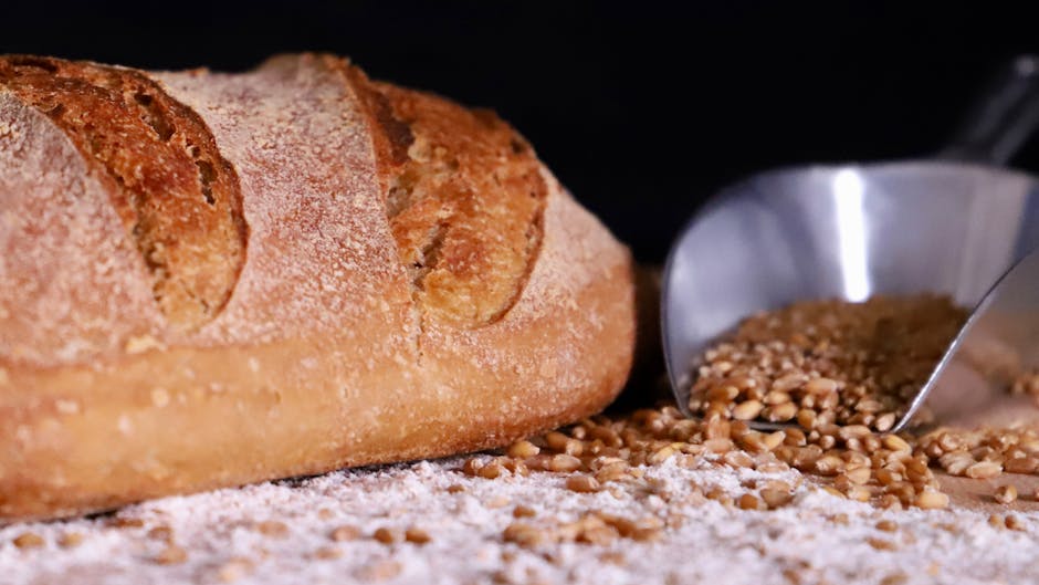 Artisan loaf of bread on a rustic surface with scattered wheat grains.