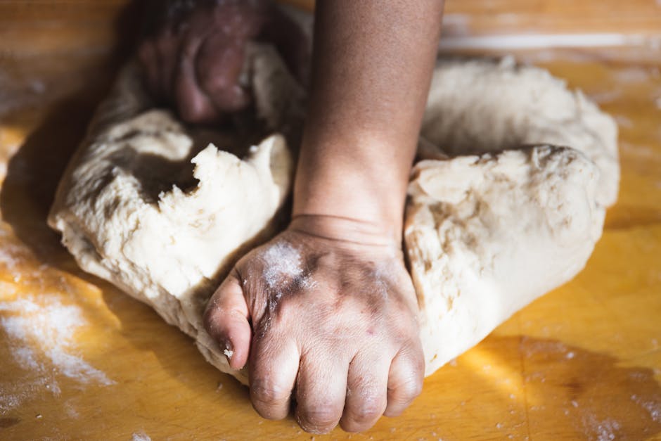 Close-up of hands kneading dough on a wooden surface, showcasing traditional baking techniques.