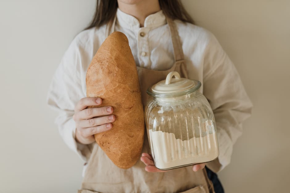 Person holding freshly baked bread and a glass jar of flour. Minimalistic style.