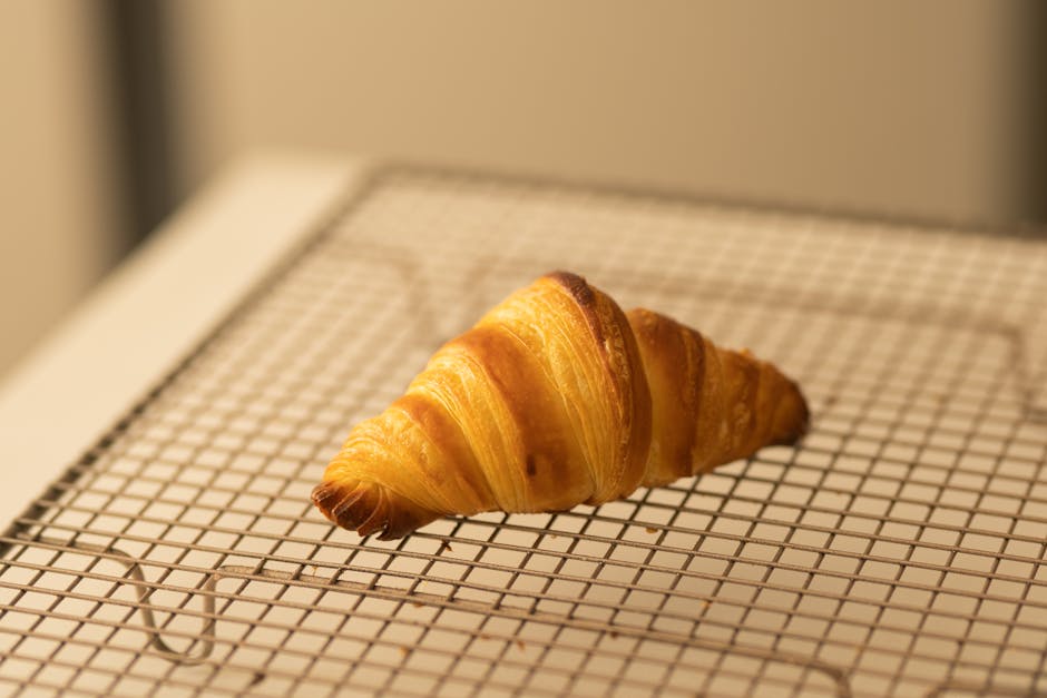 Freshly baked croissant cooling on a wire rack, showcasing golden layers and crisp texture.